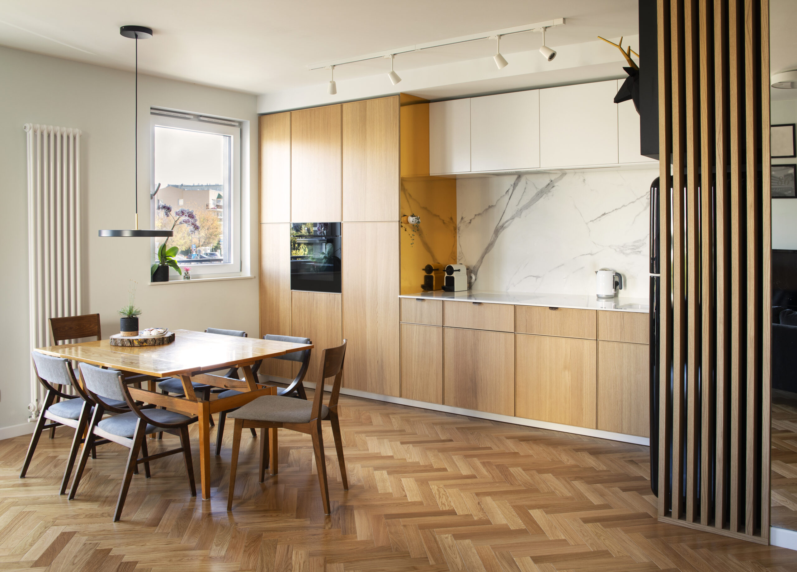Stylish scandinavian open space interior of kitchen and dining room with design family table and chairs and other kitchen and dining room accessories. Bright and sunny room with big windows and brown wooden parquet.